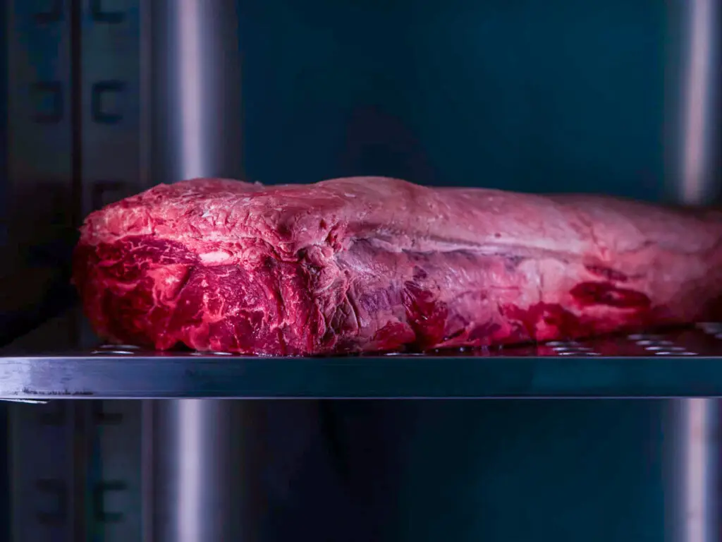 Taglio di carne rossa in fase di frollatura a secco in una cella refrigerata, processo che esalta il gusto e la tenerezza da Mestis Steakhouse Vicenza.